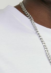 Silver metal chain necklace draped over a white cotton t-shirt with a crew neckline, showing a smooth texture and shiny links.