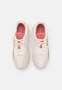 Sneaker beige chiare con mesh bianco, dettagli verdi e logo rosso. Presentano punta rotonda, dettagli perforati e lacci piatti.