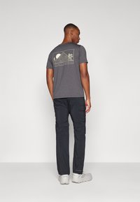 T-shirt gris à manches courtes avec un motif de montagne dans le dos. Assorti à un pantalon cargo noir et des baskets de couleur claire.