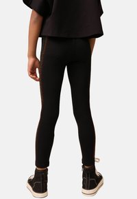 Schwarze Leggings mit einem taillierten Design, die an der Seite mit einem bunten Nietenmuster verziert sind, kombiniert mit schwarzen Mid-Top-Sneakern.