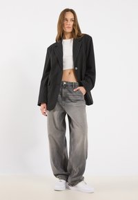 Black pinstripe blazer with a fitted design, worn over a white cropped top and paired with loose gray jeans and white sneakers.