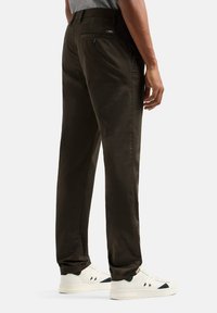 Chinos verde scuro con taglio dritto, dotati di una tasca posteriore, leggero lucido e sneakers bianche. Tessuto liscio e design pulito.