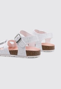 Las sandalias grises texturizadas cuentan con una correa ajustable con hebilla, una plantilla rosa y una suela de corcho marrón con detalles blancos.