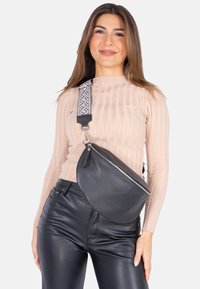 Schwarze Leder Hüfttasche mit einer geschwungenen Form, ausgestattet mit einem silbernen Reißverschluss. Die Riemen haben ein geometrisches Schwarz-Weiß-Muster, das einen Kontrast bietet.