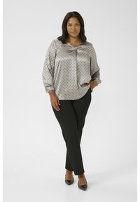 Blouse à pois gris clair avec un décolleté en V et des manches longues froncées, associée à un pantalon noir et des chaussures noires à bout pointu.