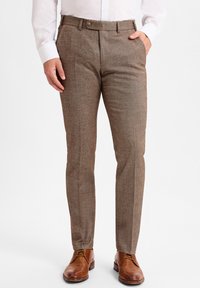 Braune, strukturierte Anzughosen mit taillierter Passform, mit flachem Frontbereich und seitlichen Taschen, kombiniert mit hellbraunen Lederschuhen.
