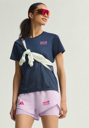 T-shirt de sport bleu marine avec un graphisme texturé et un logo "BMW Berlin Marathon" en rose, associé à un short violet clair portant le même logo et des accents roses.