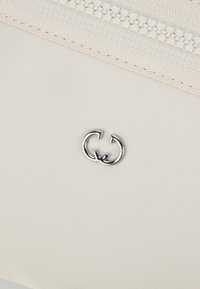 Borsa in nylon beige con un prominente logo doppio G argentato e chiusura zip testurizzata nella parte superiore, con dettagli di cucitura sottili.
