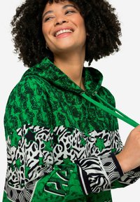 Felpa verde con cappuccio caratterizzata da diversi motivi: paisley, stelle e stampa animale. Il materiale sembra morbido con una finitura texturizzata e cappuccio regolabile.