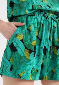 Gröna och gula shorts med bladmönster på svart bakgrund, med resårmidja och sidofickor. Slät tygtextur.