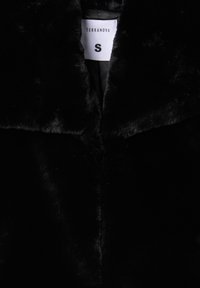 Cappotto in pelliccia sintetica nera con una texture lucida, presenta un colletto ampio e un'etichetta interna con la scritta "Terranova" e la taglia "S."
