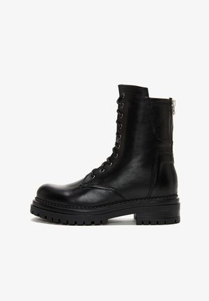 Black leather ankle boot with a rounded toe, front laces, side zipper, and thick black rubber sole with treads. Smooth texture and minimal stitching.