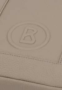 Primo piano di pelle beige testurizzata con cucitura e logo circolare in rilievo che presenta la lettera B.