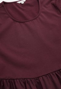 Burgundy mekko, jossa on pyöreä kaula-aukko, sileä kangas ja kellotettu, poimittu helma. Materiaali on pehmeää ja siinä on hienovarainen rakenne.