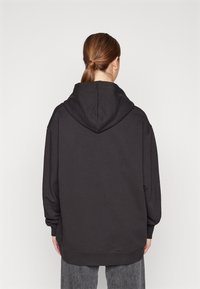 Felpa nera oversize con cappuccio regolabile, polsini a costine e orlo dritto, realizzata in morbido cotone. Dettaglio in tessuto testurizzato sul retro.