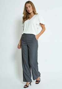 Top bianco a scollo a V con maniche a balza abbinato a pantaloni grigi a gamba dritta a vita alta. Sandali neri con tacco completano il look.