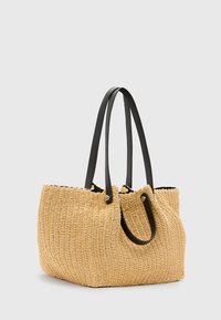 Borsa a spalla beige intrecciata con due lunghe maniglie in pelle nera e forma rettangolare ampia su sfondo grigio chiaro.