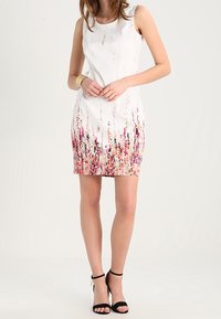 Robe blanche sans manches avec un motif dégradé coloré en teintes de rose et de violet au niveau de l'ourlet. Silhouette ajustée, tissu lisse et longueur au-dessus du genou.