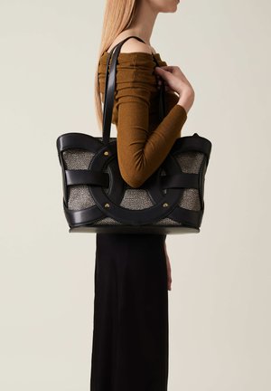 Borsa tote nera con texture intrecciata, dotata di doppi manici, design con ritagli circolari e dettagli in oro. Presenta una silhouette slanciata.