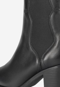 Bottine en cuir noir avec des panneaux latéraux élastiques, bout arrondi et un talon épais. Texture lisse avec des détails de couture visibles.