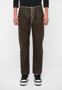 Rjave teksturirane hlače z elastičnim pasom in vrvico, ki vsebujejo dva sprednja žepa ter sproščen kroj, v kombinaciji z črnimi in belimi športnimi copati.