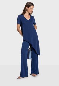 Top azul marino de manga corta con escote en V y bajo asimétrico combinado con pantalones de pierna ancha. La modelo sostiene un bolso azul claro.