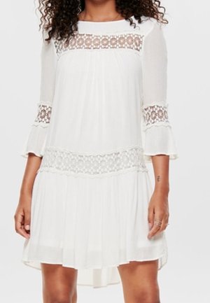 Witte jurk met driekwart transparante mouwen, kanten details bij de halslijn en taille, vloeiende silhouet en een high-low zoom.