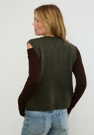 Grüner gestrickter ärmelloser Pullover mit gerippten Kanten, getragen über einem braunen Langarmshirt. Die Rückansicht zeigt einen lässigen Schnitt und einen strukturierten Stoff.