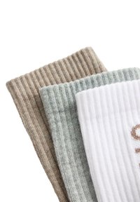 Trois pièces de tissu en maille côtelée pliées en beige, gris et blanc, empilées sur un fond blanc, montrant le contraste de texture et de couleur.