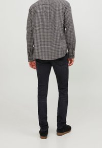 Schwarz-weiß kariertes Hemd mit langen Ärmeln, abgerundetem Saum, Knopfverschluss, kombiniert mit dunklen Slim-Fit-Jeans und schwarzen Schuhen.