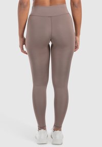 Leggings marroni a vita alta realizzati in materiale elastico, con una texture liscia e un design aderente, che si estendono fino alla caviglia.