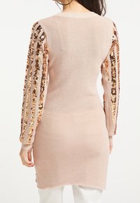 Ljust rosa stickad långärmad tröja med paljetter broderade på ärmarna och sidospalter, med en ribbad textur och rundad halsringning.