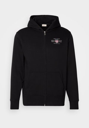 Svart zip-up hoodie i bomullsblandning, med en frontfickor, ribbade ärmslut och en logo på bröstet med röda och vita detaljer.