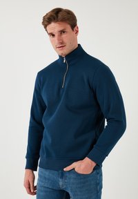 Sudadera azul marino con cuello alto y media cremallera, hecha de una tela suave, con mangas largas y puños acanalados.