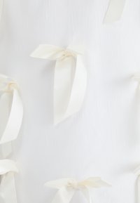 White fabric backdrop with multiple small, off-white satin bows tied at intervals, featuring a smooth texture and subtle sheen.