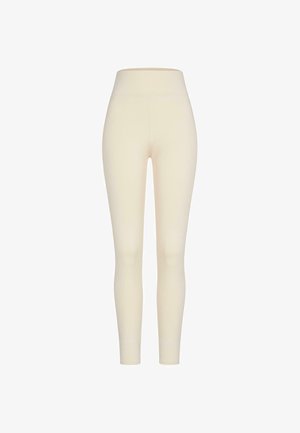 Krém színű, sima, puha textúrájú leggings, magas derékkal, amelynek testhez simuló fazonja a bokáknál szűkül.