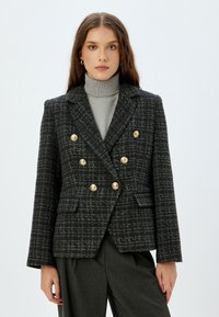 Zwart en grijs geblokte blazer met dubbelgeknoopte goudkleurige knopen, gekartelde revers en twee voorzakken, van een gestructureerde geweven stof.