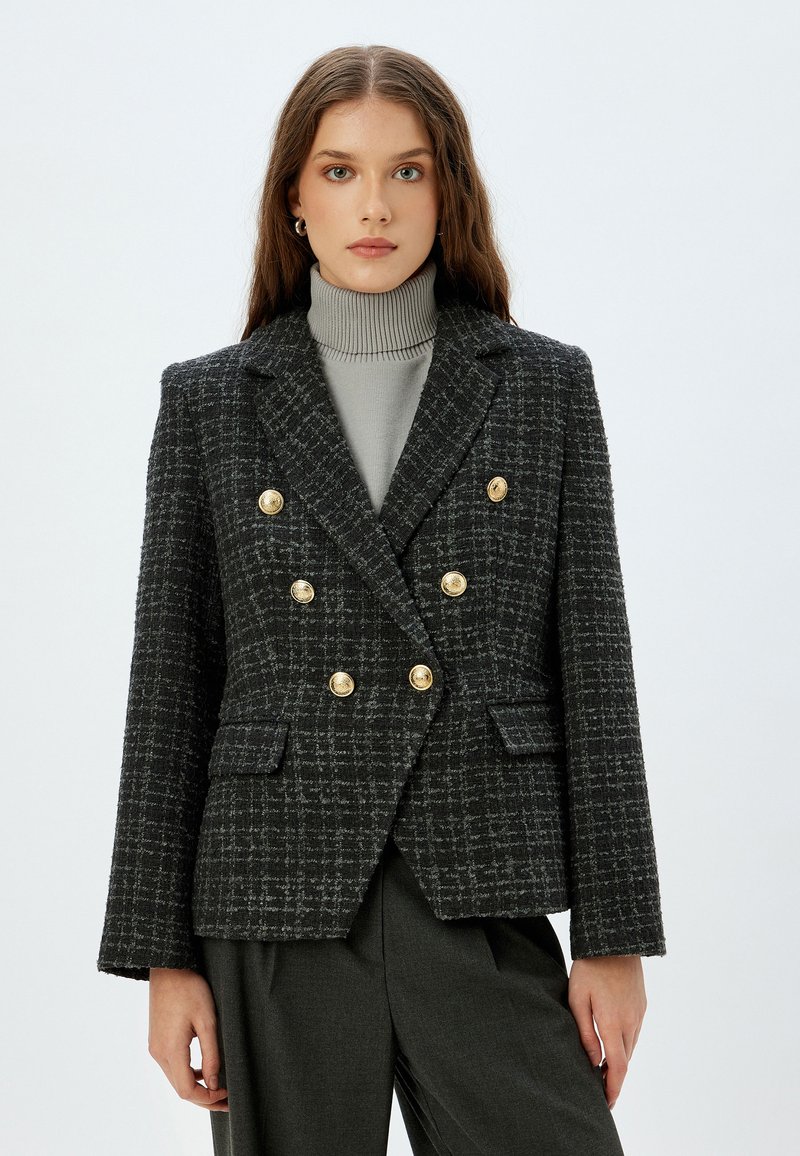 Zwart en grijs geblokte blazer met dubbelgeknoopte goudkleurige knopen, gekartelde revers en twee voorzakken, van een gestructureerde geweven stof.