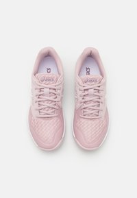 Tênis esportivos rosa claro com tecido de malha, colarinhos acolchoados e solas brancas. Apresenta atacadores, logotipo e padrões texturizados na parte superior.
