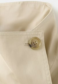 Col de tissu beige avec un grand bouton brun translucide fixé à travers une boutonnière cousue.