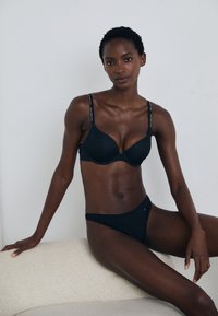Juodas liemenukas su formuotais puodeliais ir reguliuojamomis petnešomis, derinamas su atitinkamomis bikini kelnaitėmis. Abu daiktai turi lygų tekstūrą ir minimalistinį dizainą.