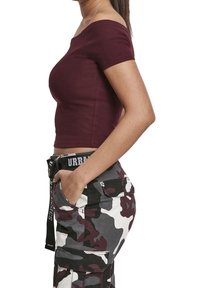 Ribbade burgunderfärgade off-shoulder topp parat med kamouflage cargo byxor med flera fickor och ett svart bälte med vit text.