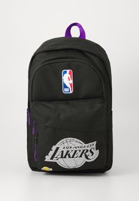 Mochila preta com o logo da NBA e gráfico dos "Los Angeles Lakers". Apresenta detalhes em roxo nos fechos e uma pega na parte de cima para transporte.