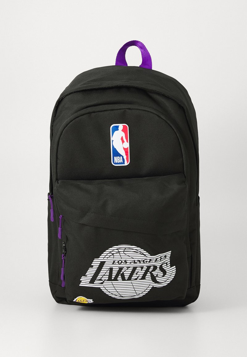 Mochila preta com o logo da NBA e gráfico dos "Los Angeles Lakers". Apresenta detalhes em roxo nos fechos e uma pega na parte de cima para transporte.