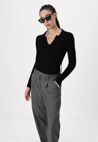 Haut noir à rayures, à manches longues, avec un col en V, associé à un pantalon gris taille haute. Les accessoires comprennent un collier en chaîne en argent et des lunettes de soleil noires.