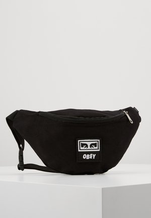 Sac banane en tissu noir avec fermeture éclair et un patch logo à l’avant indiquant "OBEY" avec des yeux stylisés.