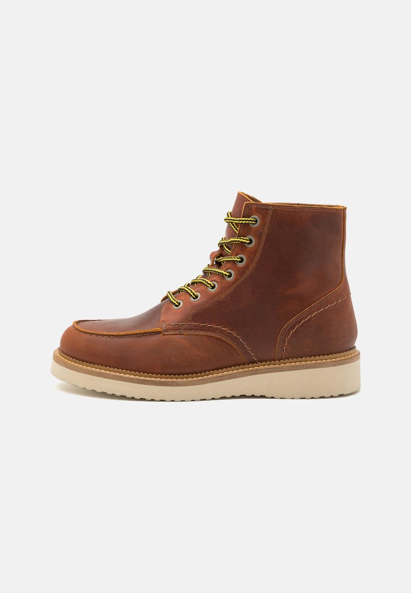 Stivale in pelle marrone alla caviglia con punta rotonda, suola in gomma beige e lacci gialli. Presenta cuciture a contrasto e un colletto imbottito.