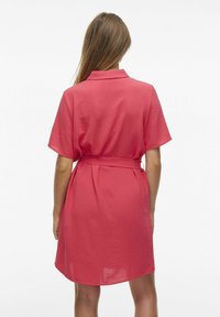 Krátkoná rukáv, polo šaty v žiarivej koralovej farbe so zaväzovaním v páse a textúrovanou tkaninou. Siahajú tesne nad kolená a poskytujú uvoľnený strih.