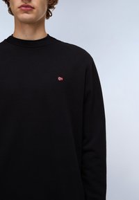 Hanorac negru cu guler și manșete ribbate, având o mică broderie a steagului norvegian pe piept. Țesătură din bumbac neted.