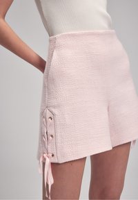 Světle růžové texturované šortky s fitted designem, s krajkovými detaily na bocích s růžovými stužkami a zlatými očky.